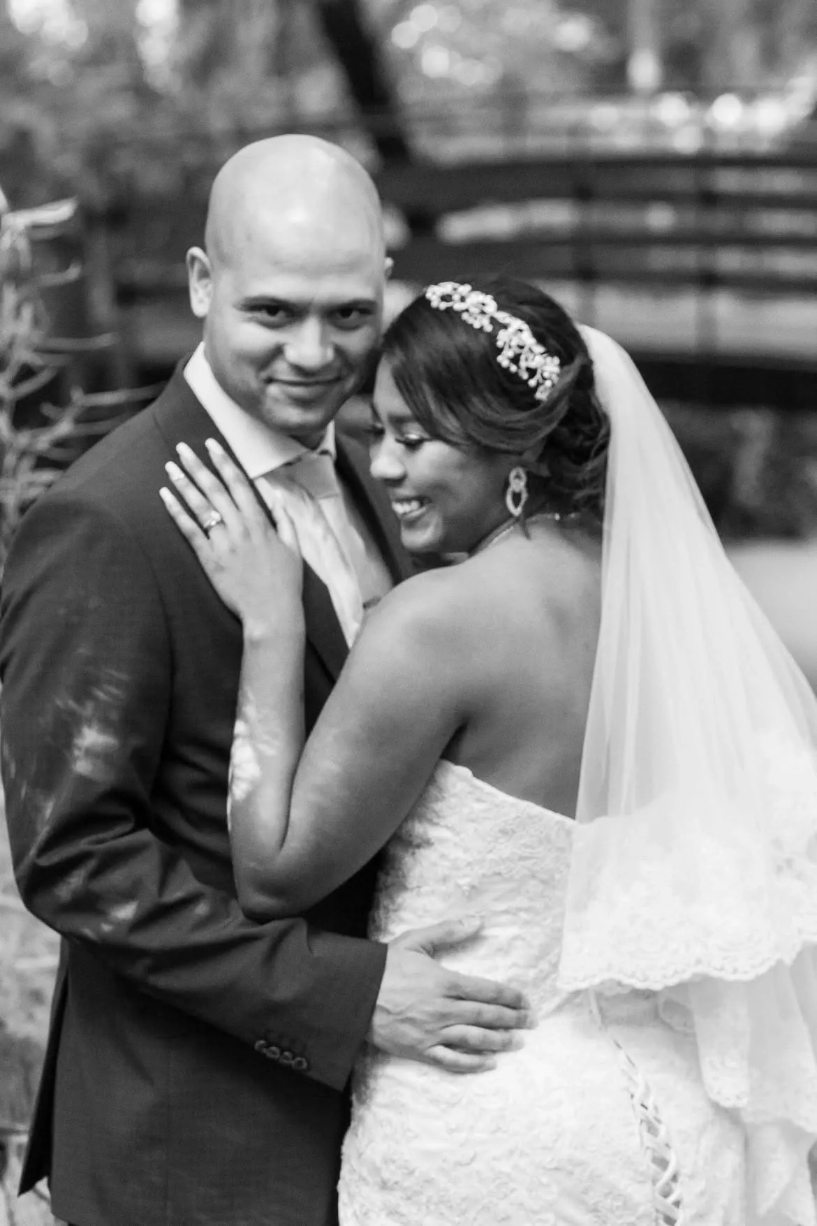 Black and white portrait of a bride with a jewelled hair comb and veil embracing her smiling groom.