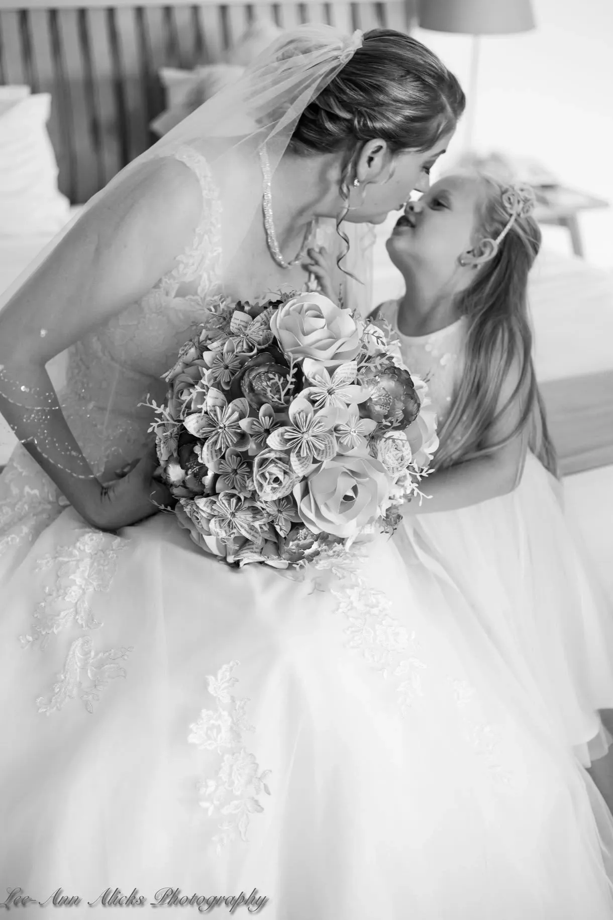 Black and white photo of a bride touching noses with the flower girl while getting ready.