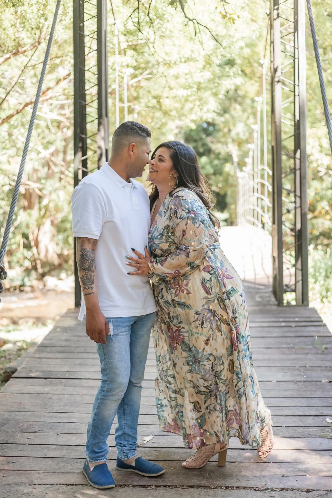 Couple leaning in close on a wooden suspension footbridge among trees.