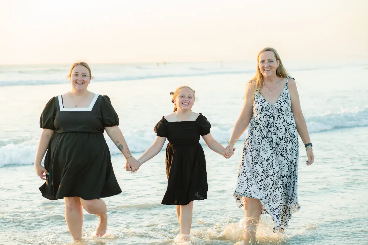 Three family members walking hand in hand through the shallows at a beach photoshoot.