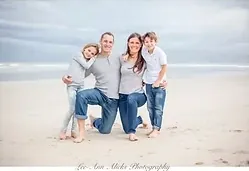 Family of four posing together on a wide sandy beach under a grey sky.