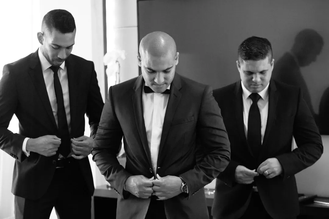Black and white photo of the groom and groomsmen buttoning their jackets before the ceremony.