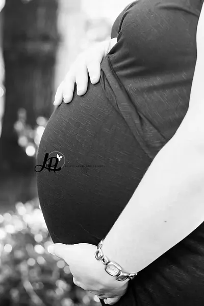 Black and white close-up of a pregnant bump with both hands resting on it.
