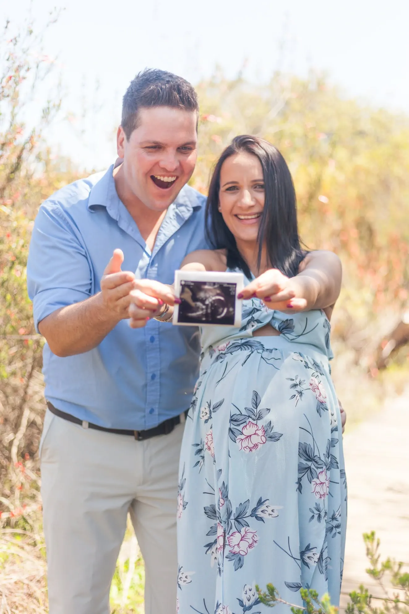 Expecting couple laughing and holding up the baby's scan photo together.
