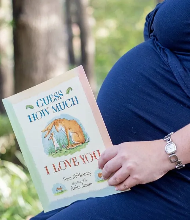 Maternity photoshoot detail: the children's book Guess How Much I Love You held against the bump.