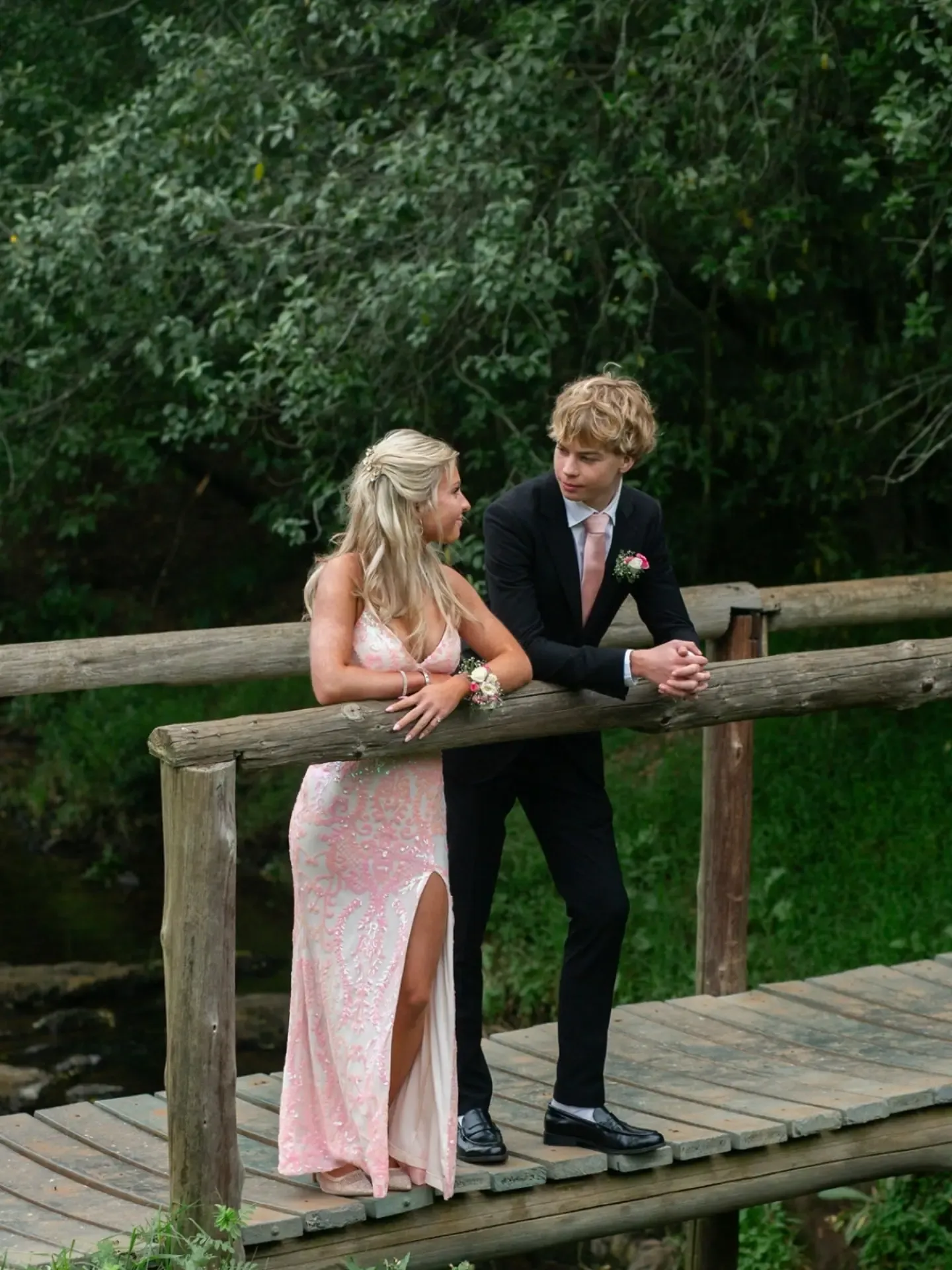 Matric dance couple leaning on a rustic wooden bridge railing.