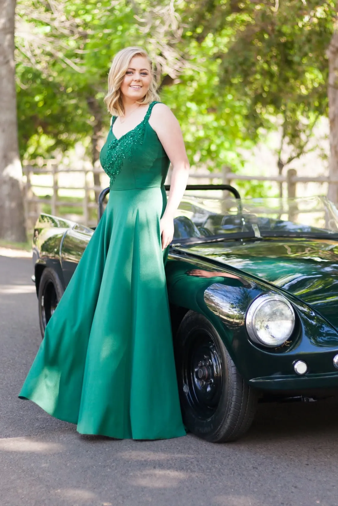 Matriculant in a long emerald gown standing beside a vintage green convertible.
