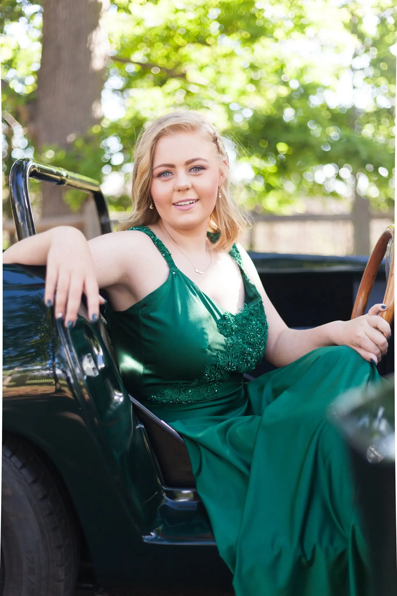 Matriculant in an emerald gown seated in a vintage green convertible.
