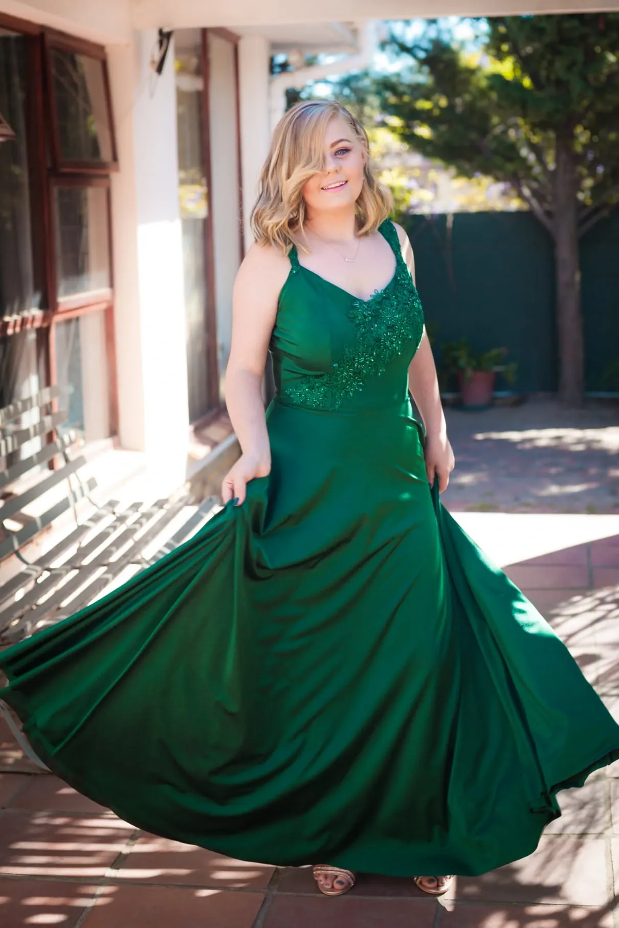 Matriculant in an emerald satin gown swirling the skirt on a sunny tiled stoep.