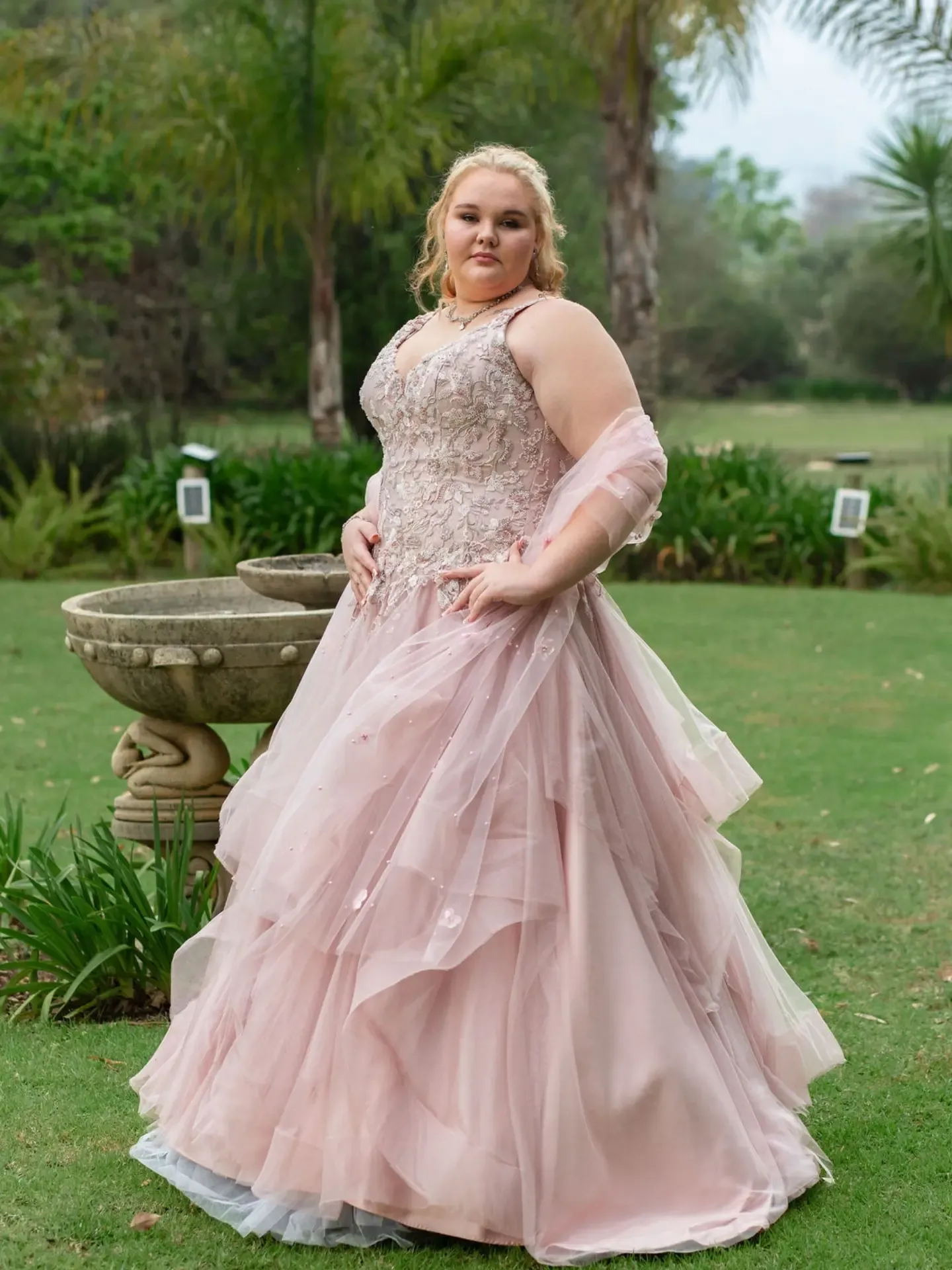 Matric dance photoshoot: matriculant in a blush-pink tulle ball gown standing on a garden lawn.