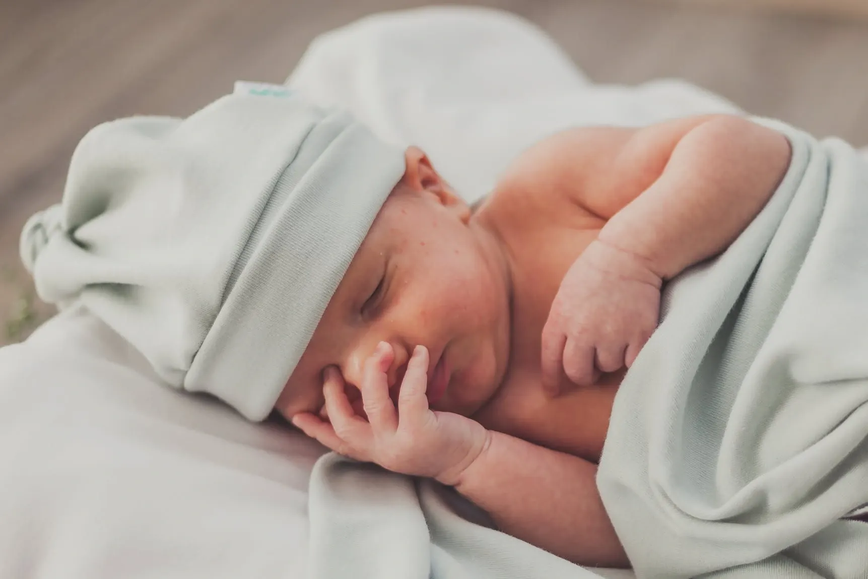 Close-up of a sleeping newborn in a soft mint hat, one hand tucked against the cheek.
