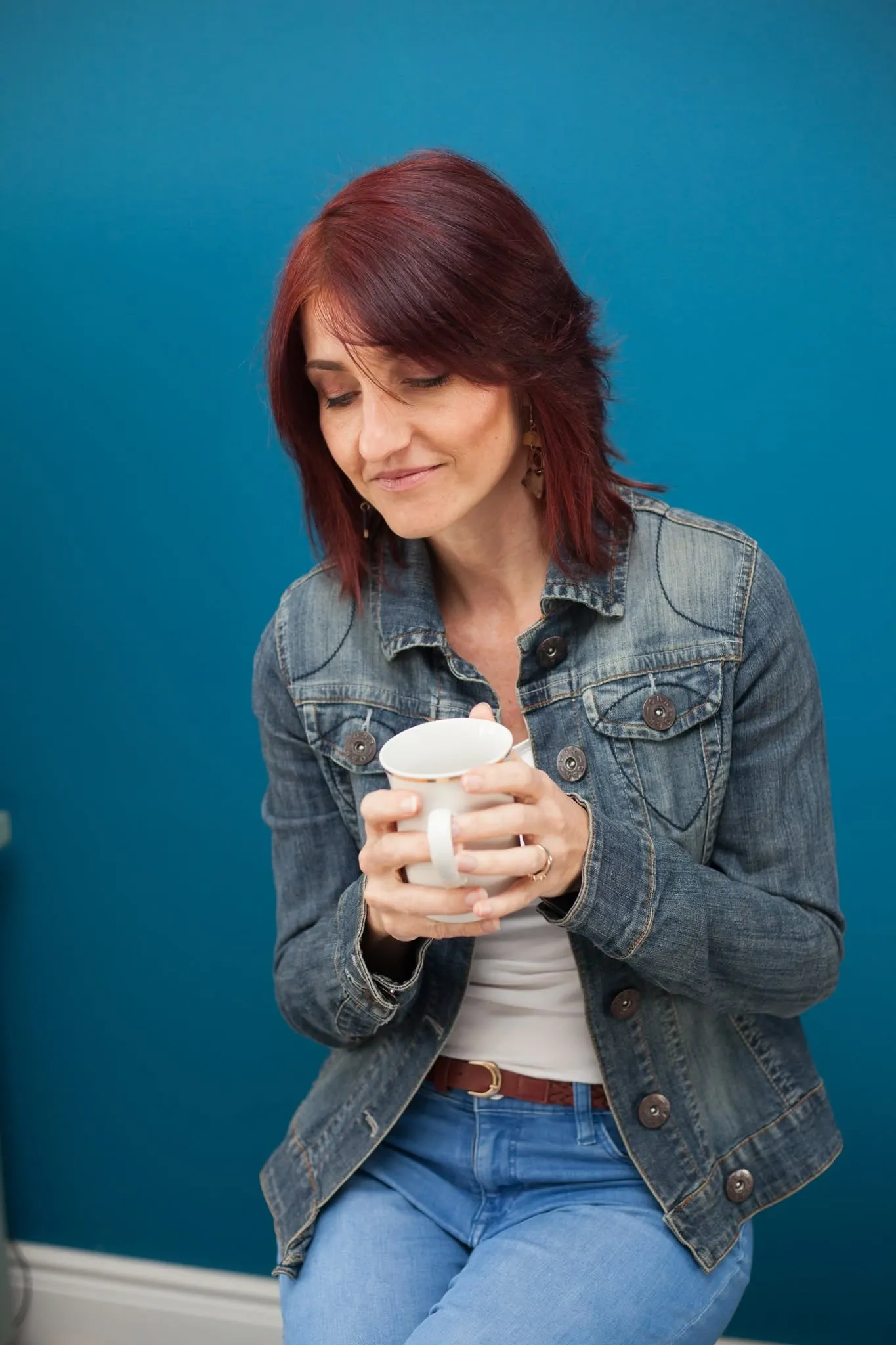 Candid personal branding portrait of a woman holding a coffee cup against a teal wall.