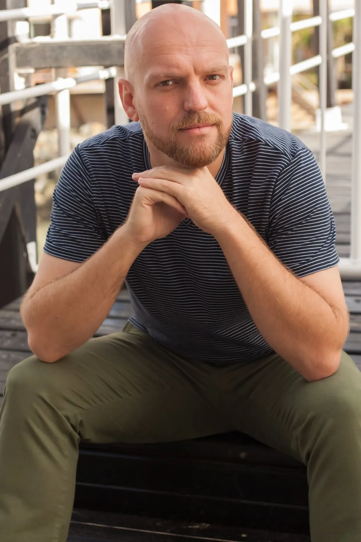 Relaxed personal branding portrait of a man seated on wooden steps, chin resting on his hands.