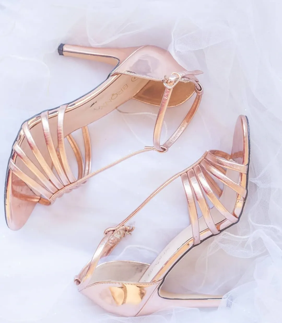 Rose-gold strappy bridal sandals lying on white tulle.