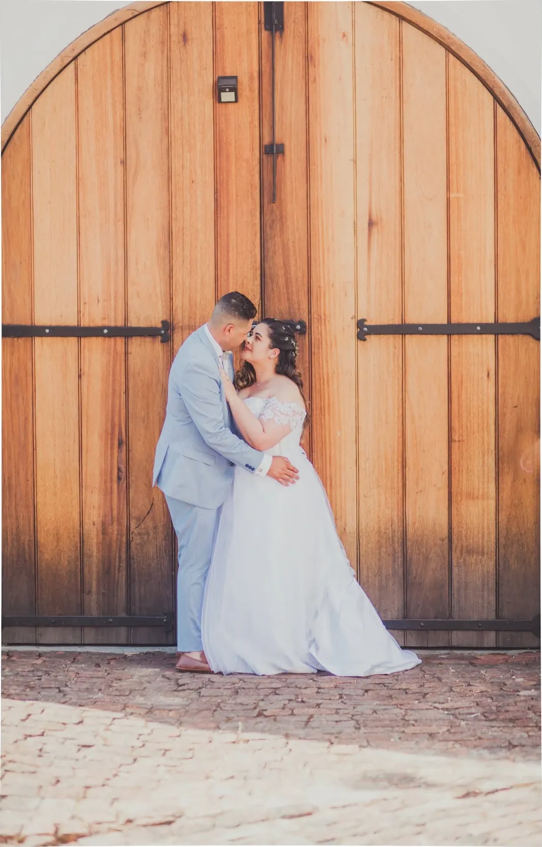 Bride and groom embracing in front of tall arched wooden doors.