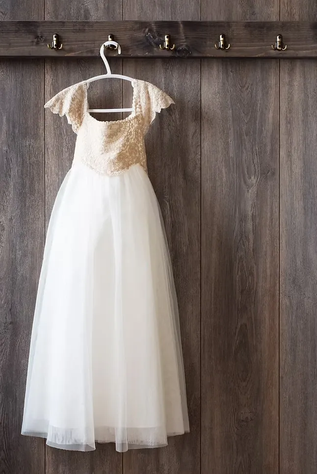 White dress with a lace bodice on a hanger, hooked to a rail on a weathered wooden wall.