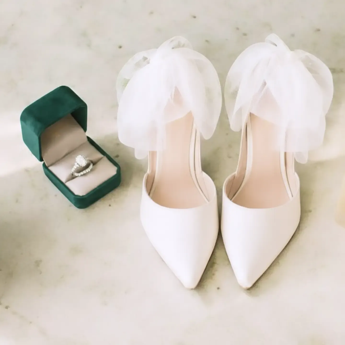 Wedding details: engagement ring in a green velvet box beside white bridal shoes with tulle bows.