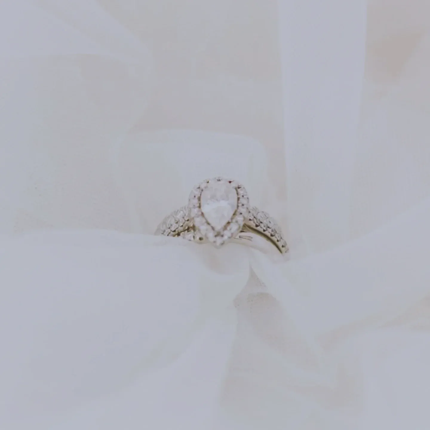 Pear-shaped engagement ring and wedding band resting in soft white tulle.